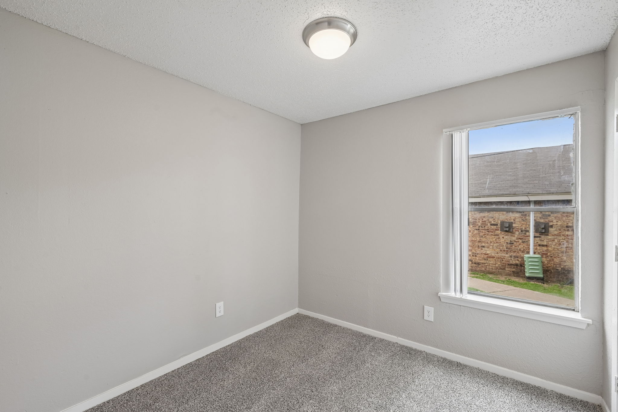 A room with a window showing a view of a building and a green post.